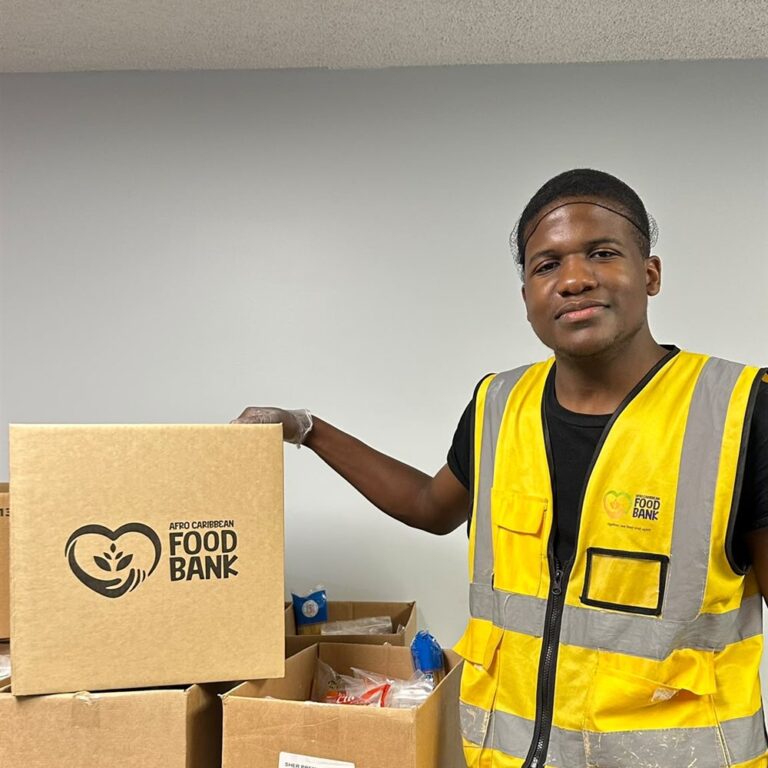ACFBCC volunteer in a safety vest standing beside branded food hamper boxes.