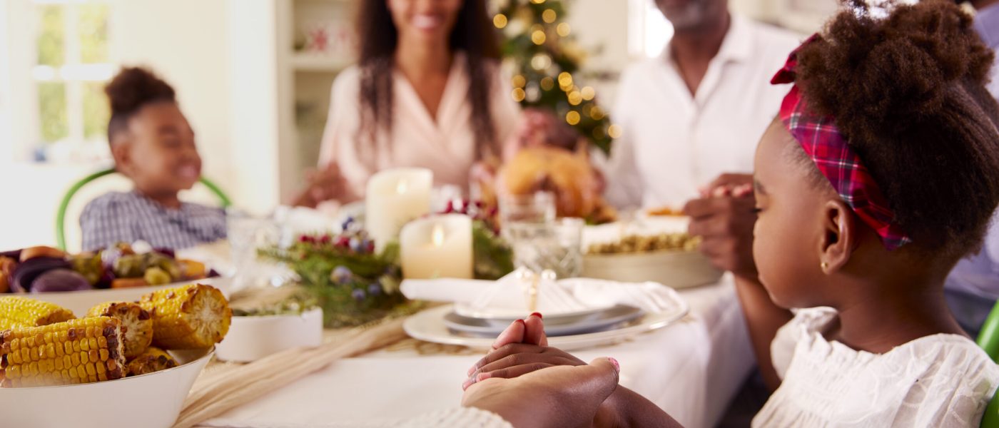 Multi-Generation Family Celebrating Christmas At Home Saying Prayer Before Eating Meal Together